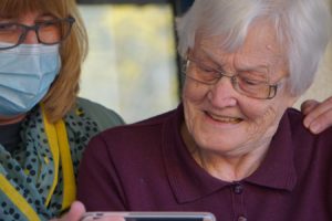 Une infirmière tenant un smartphone pour une dame âgée.